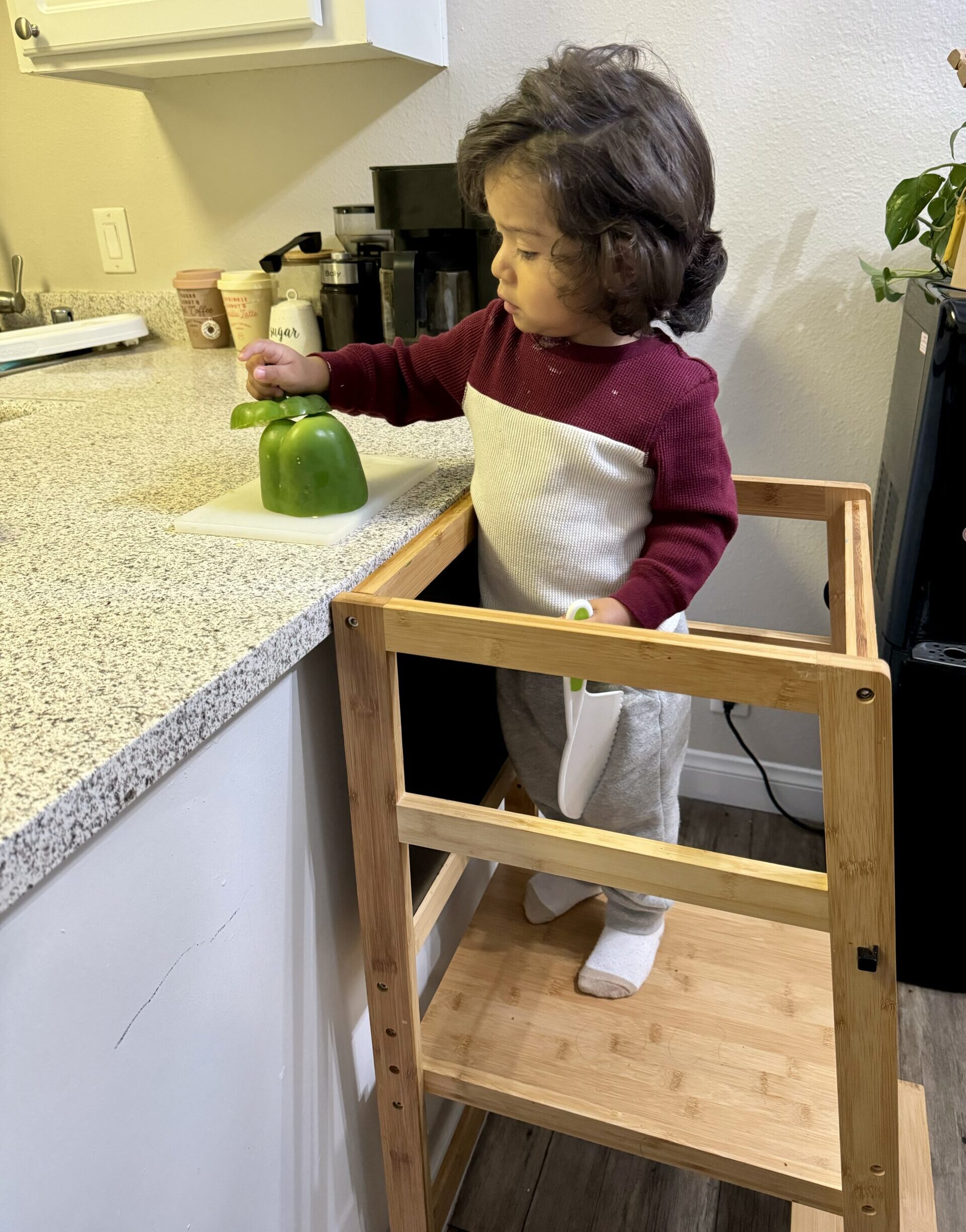 toddler cutting vegetable on a learning tower